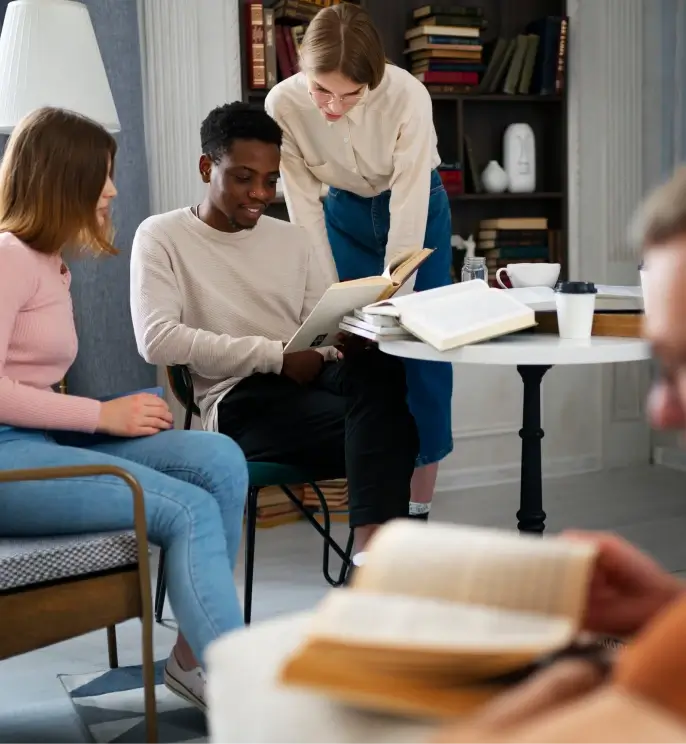 A guy and two girls are reading books by the table.