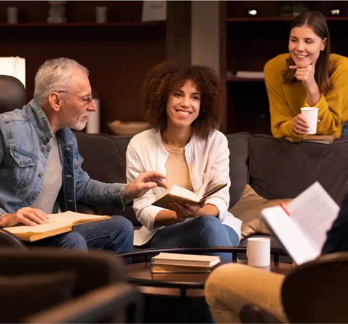 A group of people sitting in a circle reading with smiles on their faces.