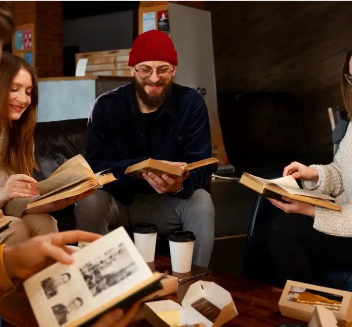 A group of people sitting in a circle reading with smiles on their faces.